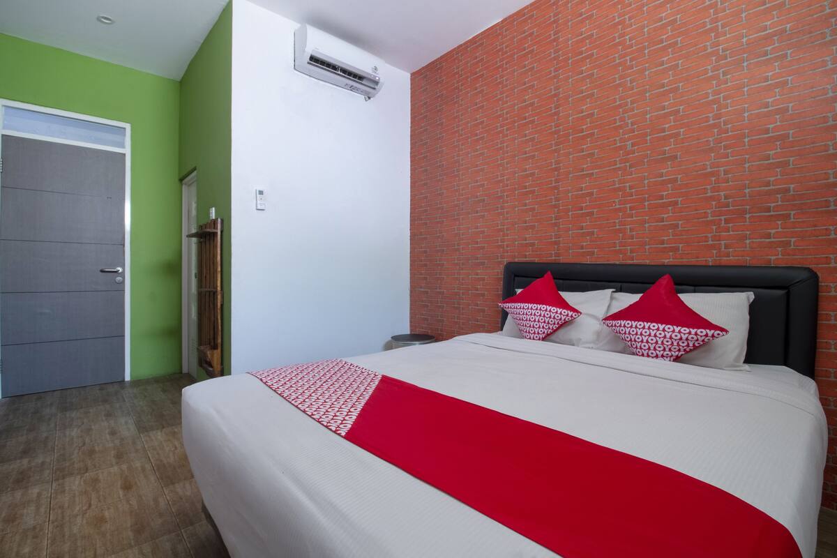 Een hotelkamer met een bed, een groene muur, een bakstenen muur en een airconditioning.