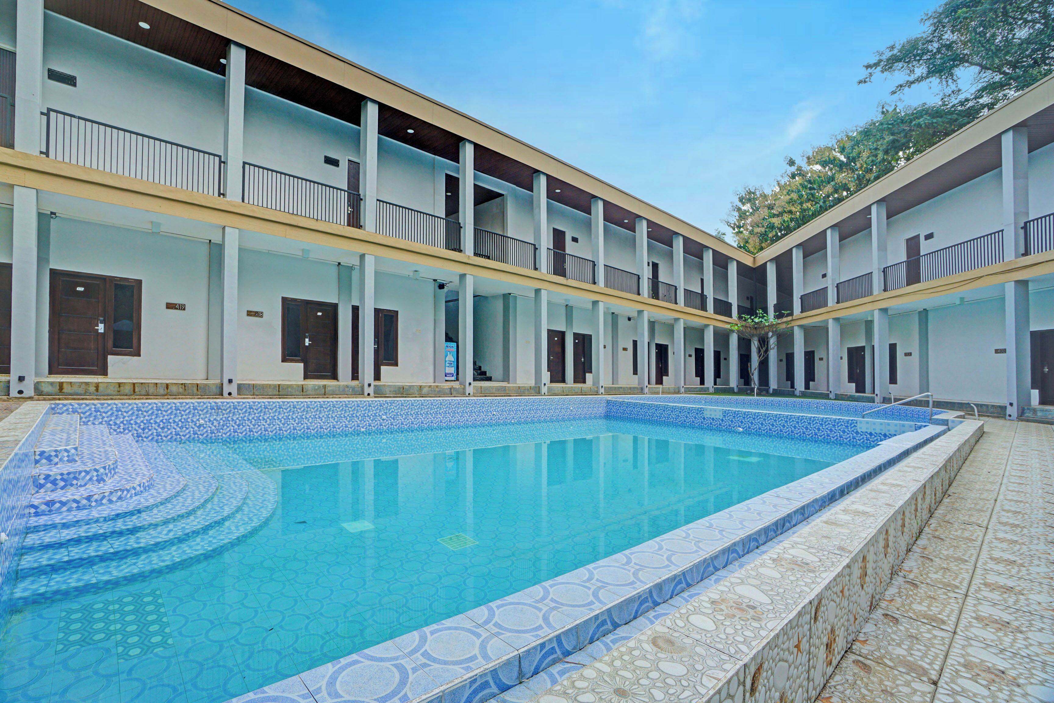 A swimming pool with a tiled edge, surrounded by a multi-story building with balconies and doors.