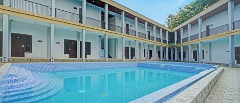 A swimming pool with a tiled edge, surrounded by a multi-story building with balconies and doors.