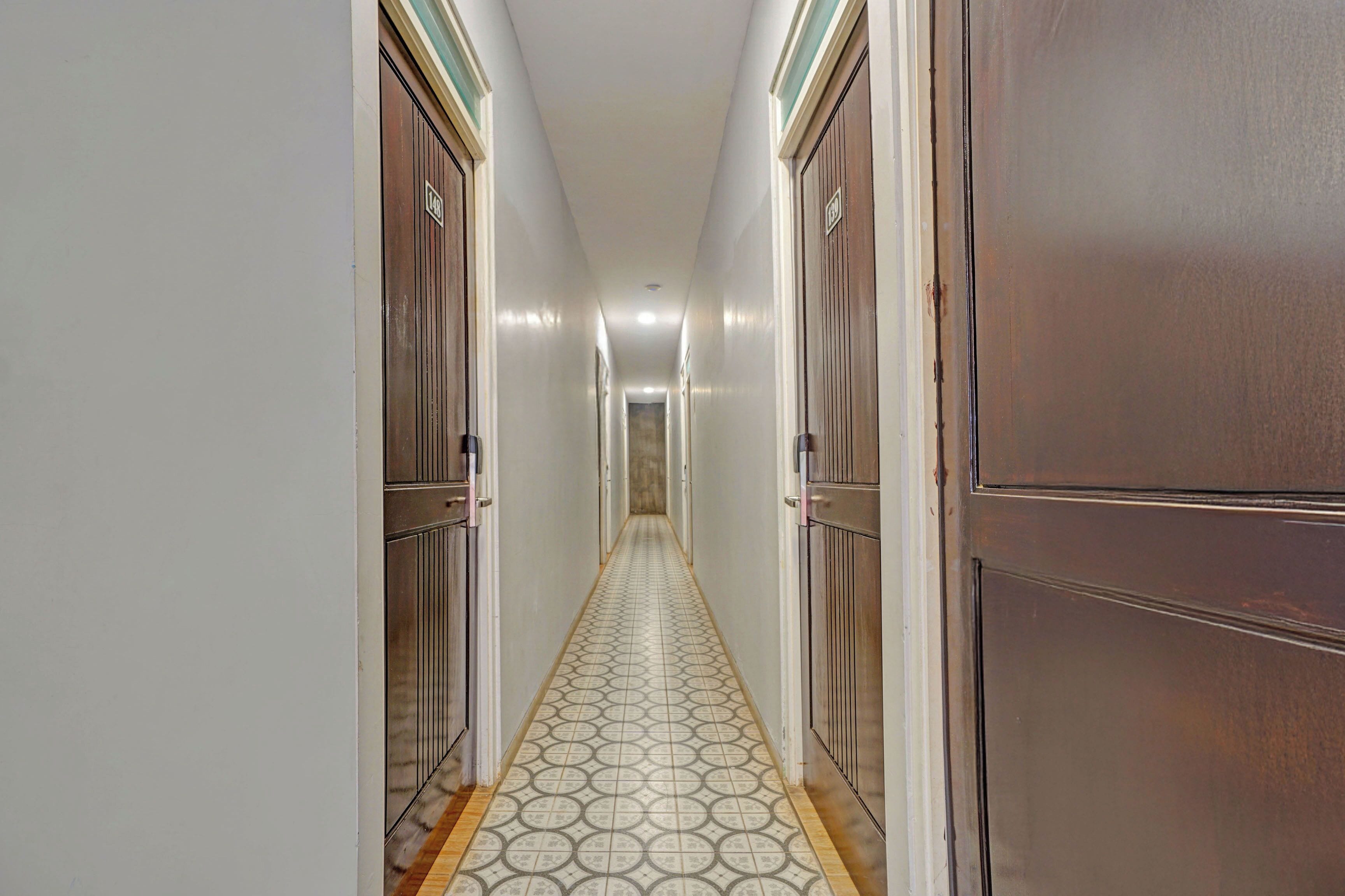 A hallway with a patterned floor, wooden doors, and a light-colored wall.