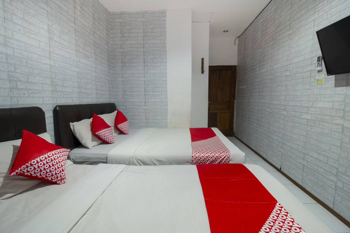 Een hotelkamer met twee bedden, witte beddengoed, kussens met een rood-wit patroon en een rood-witte deken.