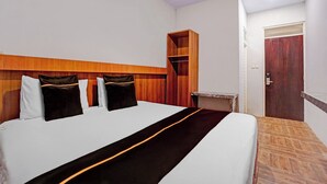 Quarto de hotel com cama, cabeceira de madeira, guarda-roupa, mesa pequena e porta.
