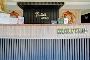 Ein Hotelrezeptionstresen mit Holzpaneelen, einem Empfangsschild und einer Wanddekoration mit Sonnenelementen.