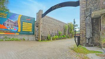 A hotel entrance with a stone facade, a large signboard, and a paved walkway.