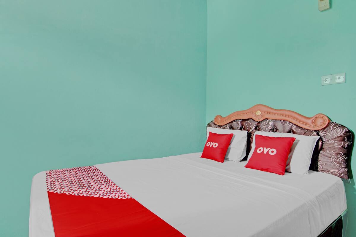 A bed with a white and red bedspread, two red pillows with the word "OYO" on them, and a wooden headboard with a patterned design.
