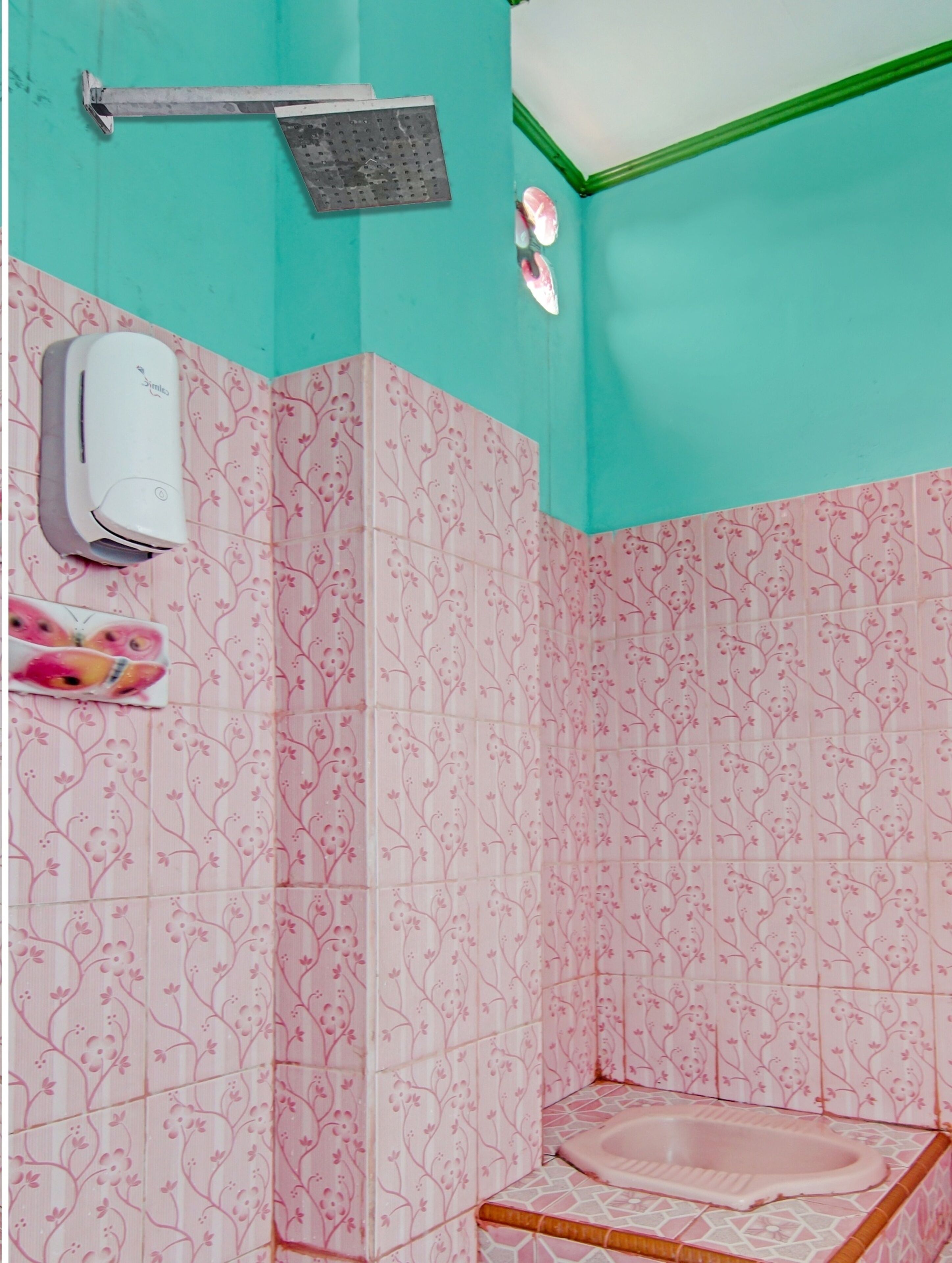 Une salle de bain avec des carreaux de céramique à motifs floraux roses, une pomme de douche, un distributeur de savon et des toilettes.