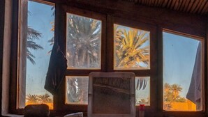 Una habitación con ventanas amplias, una cama, una mesita de noche y una pequeña mesa con lámpara.