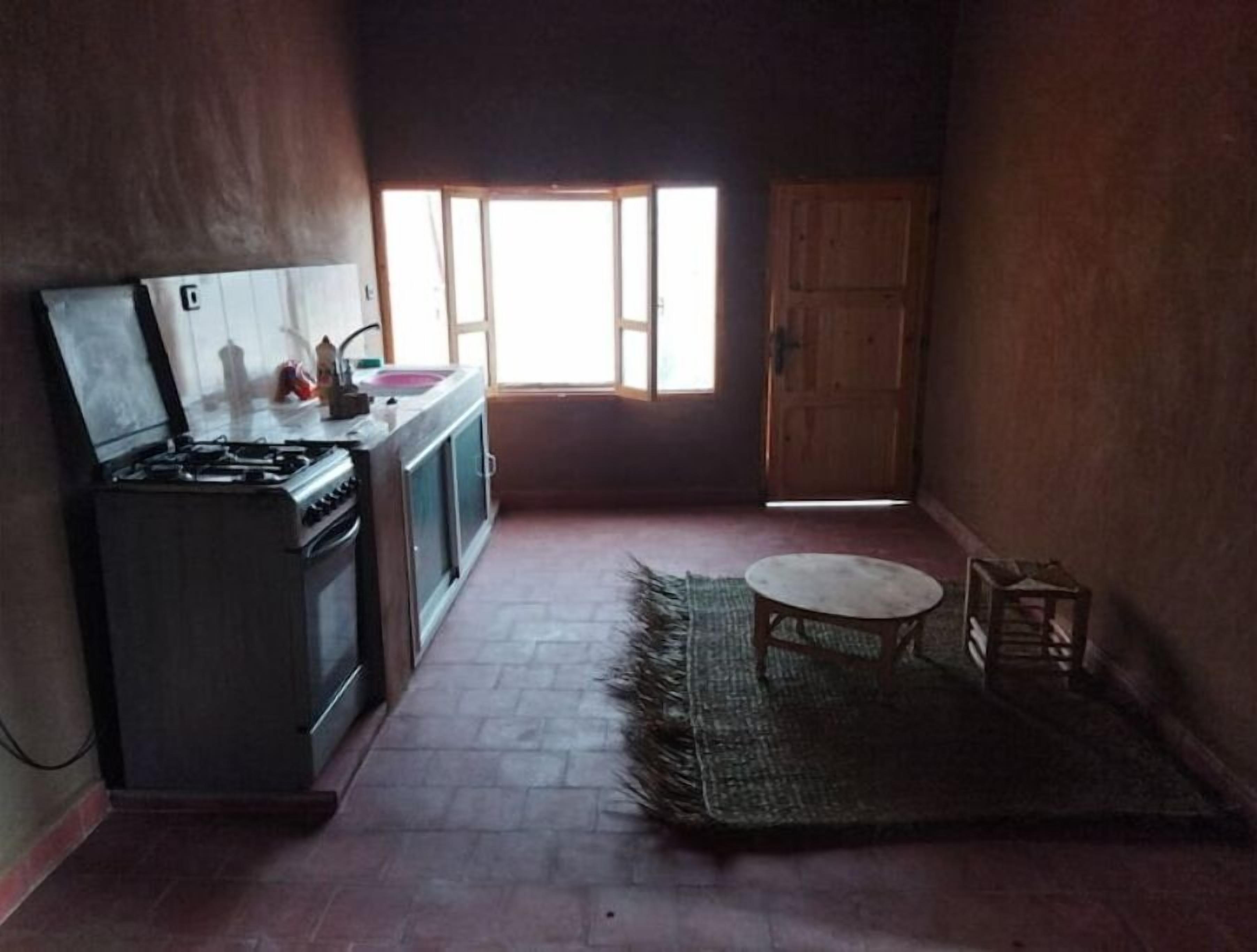 Une cuisine de taille réduite, équipée d’une cuisinière à gaz, d’un évier et d’une fenêtre laissant entrer la lumière naturelle.