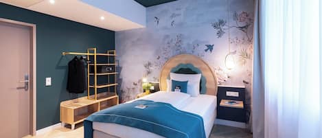 A modern bedroom with a bed, a wooden bench, a shelf unit, and a wall with floral and bird designs.