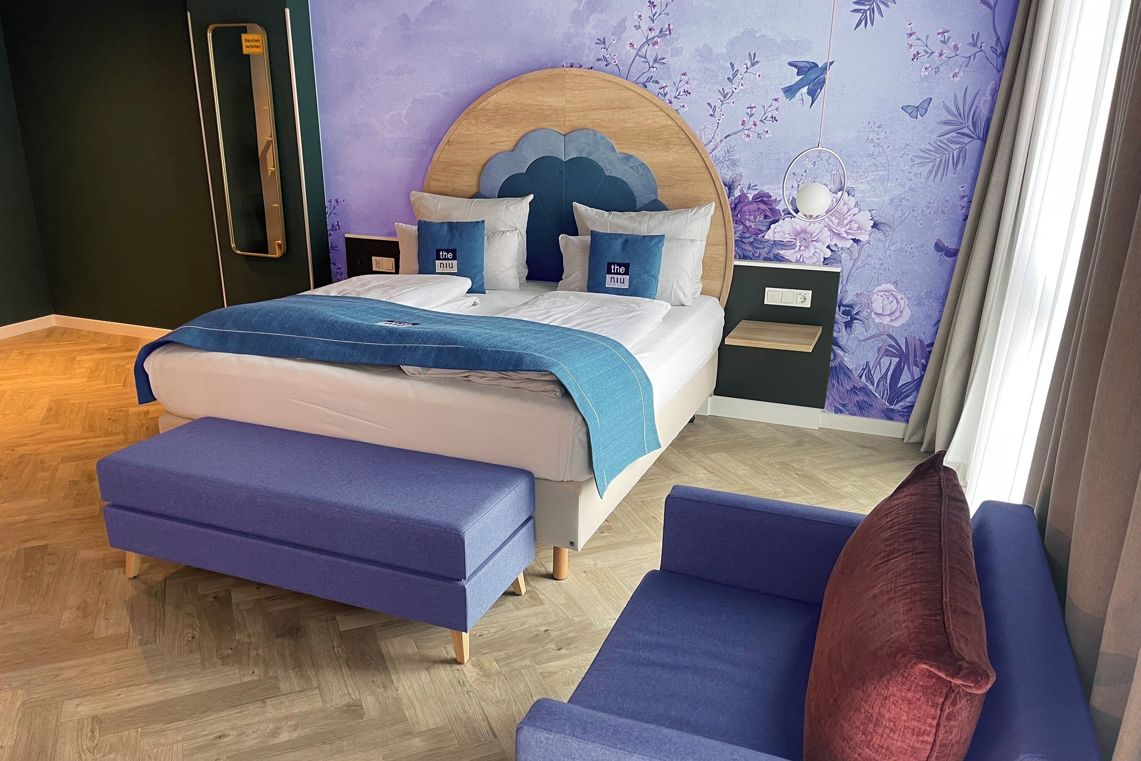 A bedroom with a bed, a wooden headboard, a nightstand, a blue bench, and a red pillow.