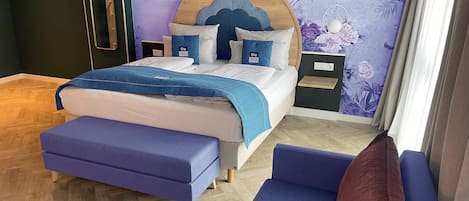 Een slaapkamer met een bed, een houten hoofdbord, een nachtkastje, een blauwe bank en een rode kussen.