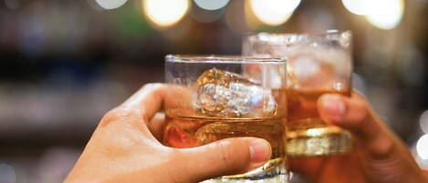 Two hands holding glasses of amber-colored beverage with ice cubes.