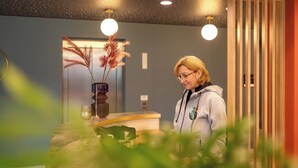 A reception desk with a vase of dried plants, a wooden panel, and a light fixture. - Holiday Inn - the niu, Flower Konstanz by IHG (Konstanz)