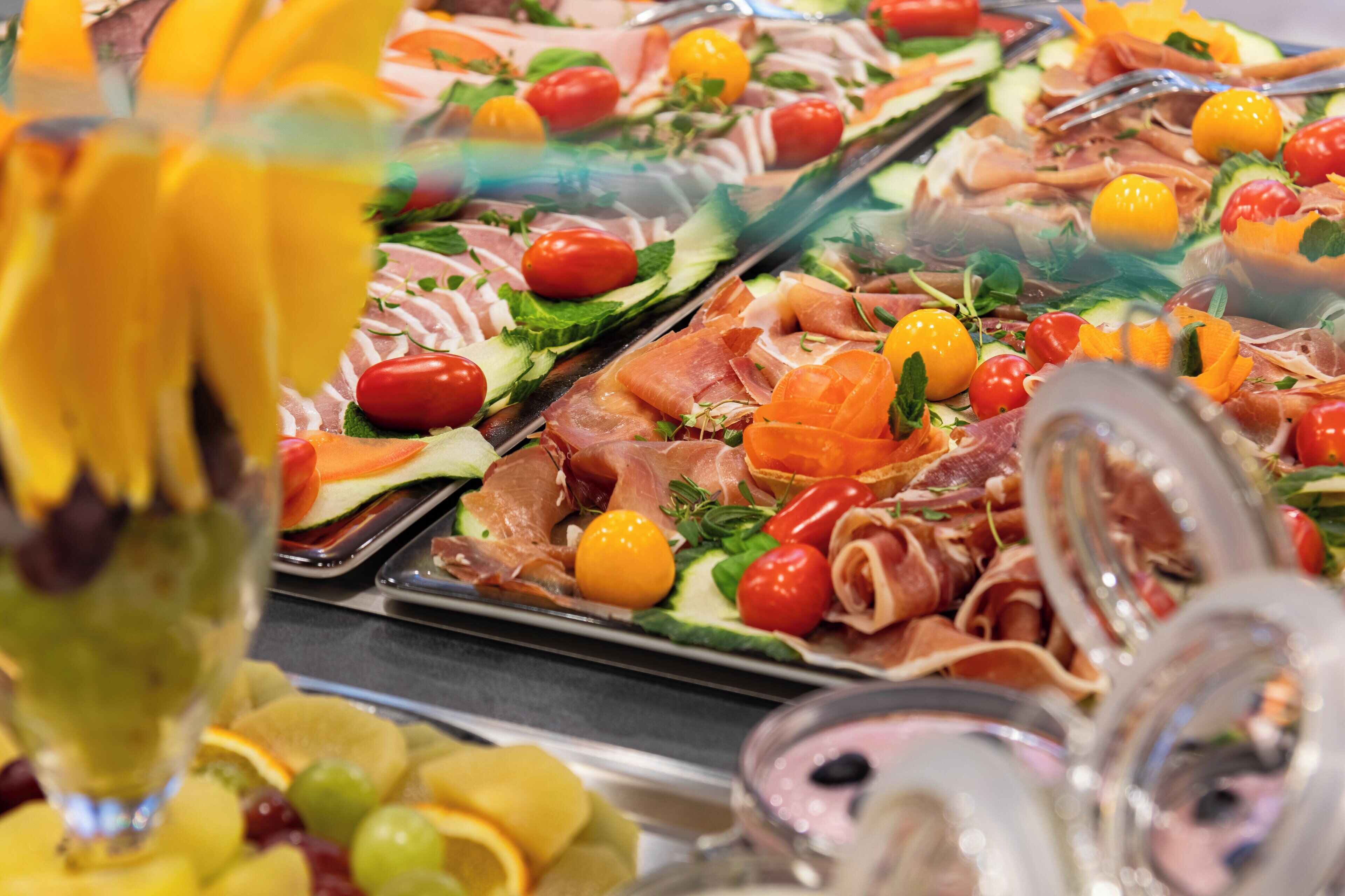 Un bufé con diversas opciones de comida, incluyendo carnes, quesos y frutas.