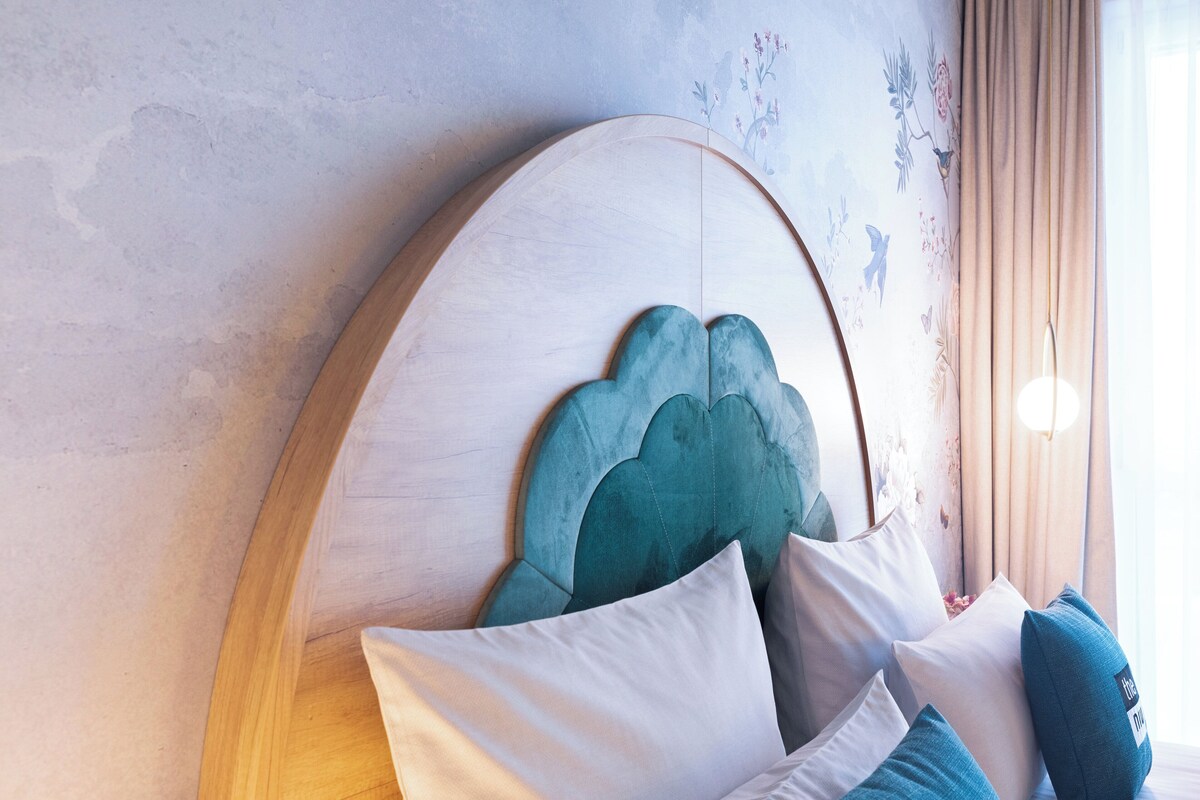 Ein Schlafzimmer mit einem Holz-Kopfteil, weißen und türkisblauen Kissen und blumigem Wandpapier.