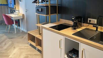 Ett modernt kök med en inbyggd spis, en kaffemaskin och en diskho. I bakgrunden finns ett skrivbord med en stol och en tv.