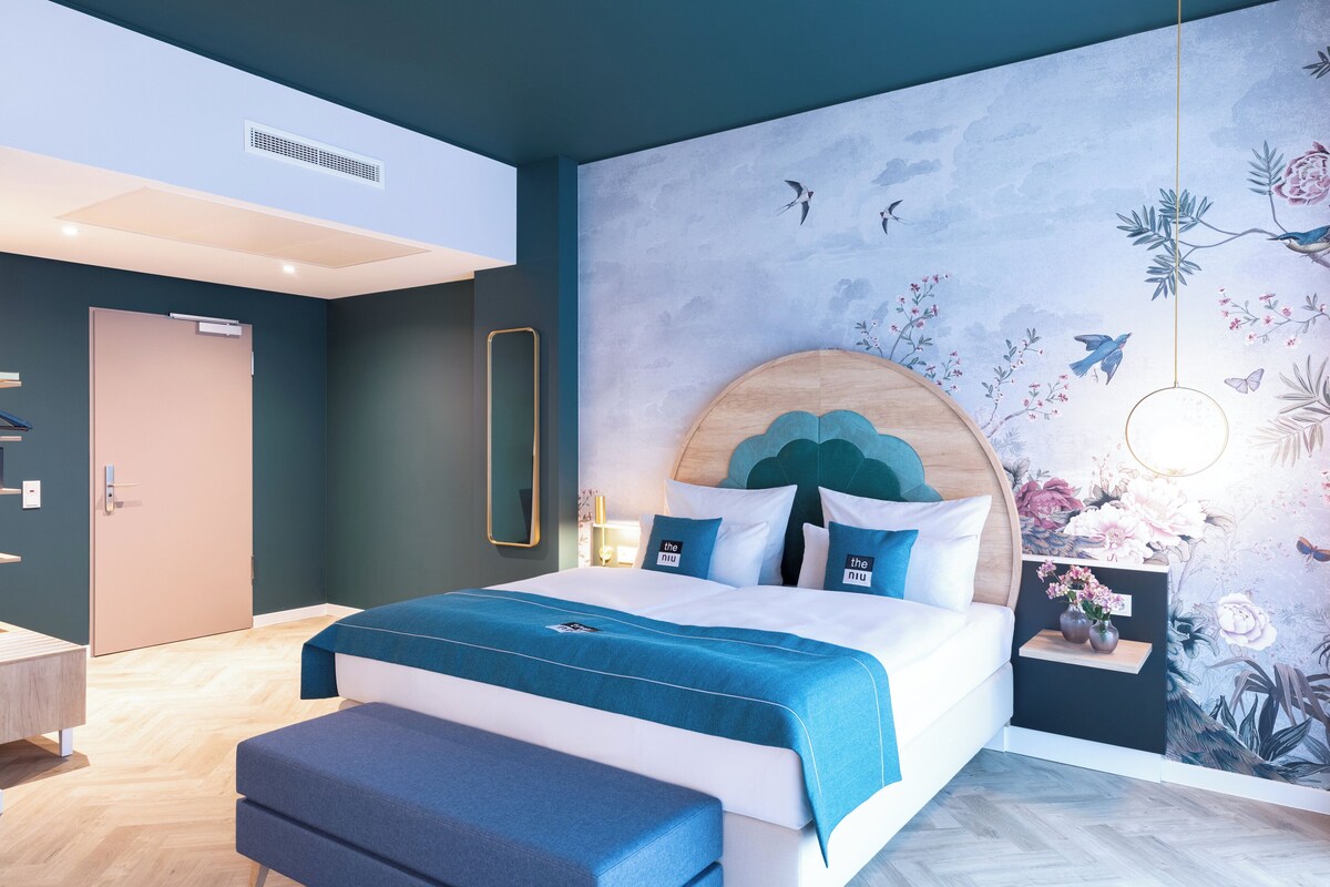 Ein modernes Schlafzimmer mit einem großen Bett, einem Holzkopfteil und einer Wandmalerei mit Vögeln und Blumen.