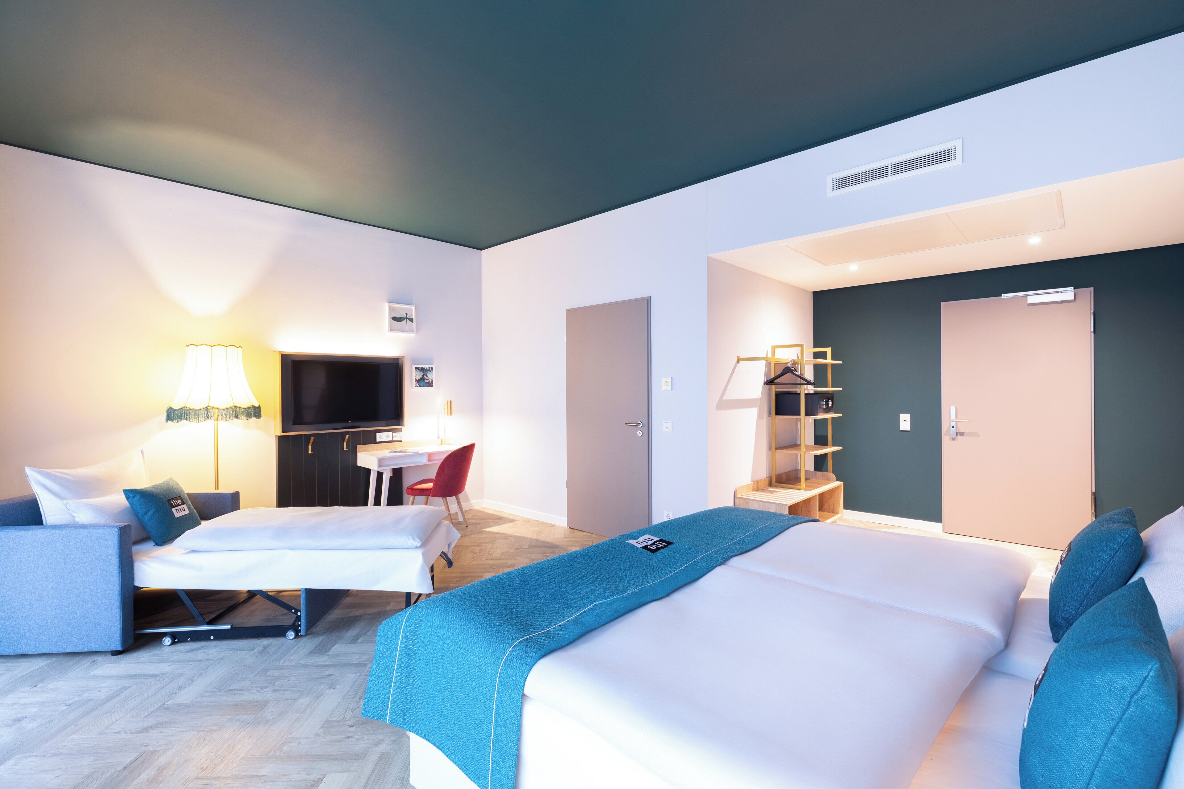 Una habitación de hotel moderna con dos camas, un escritorio, un televisor y una silla roja.