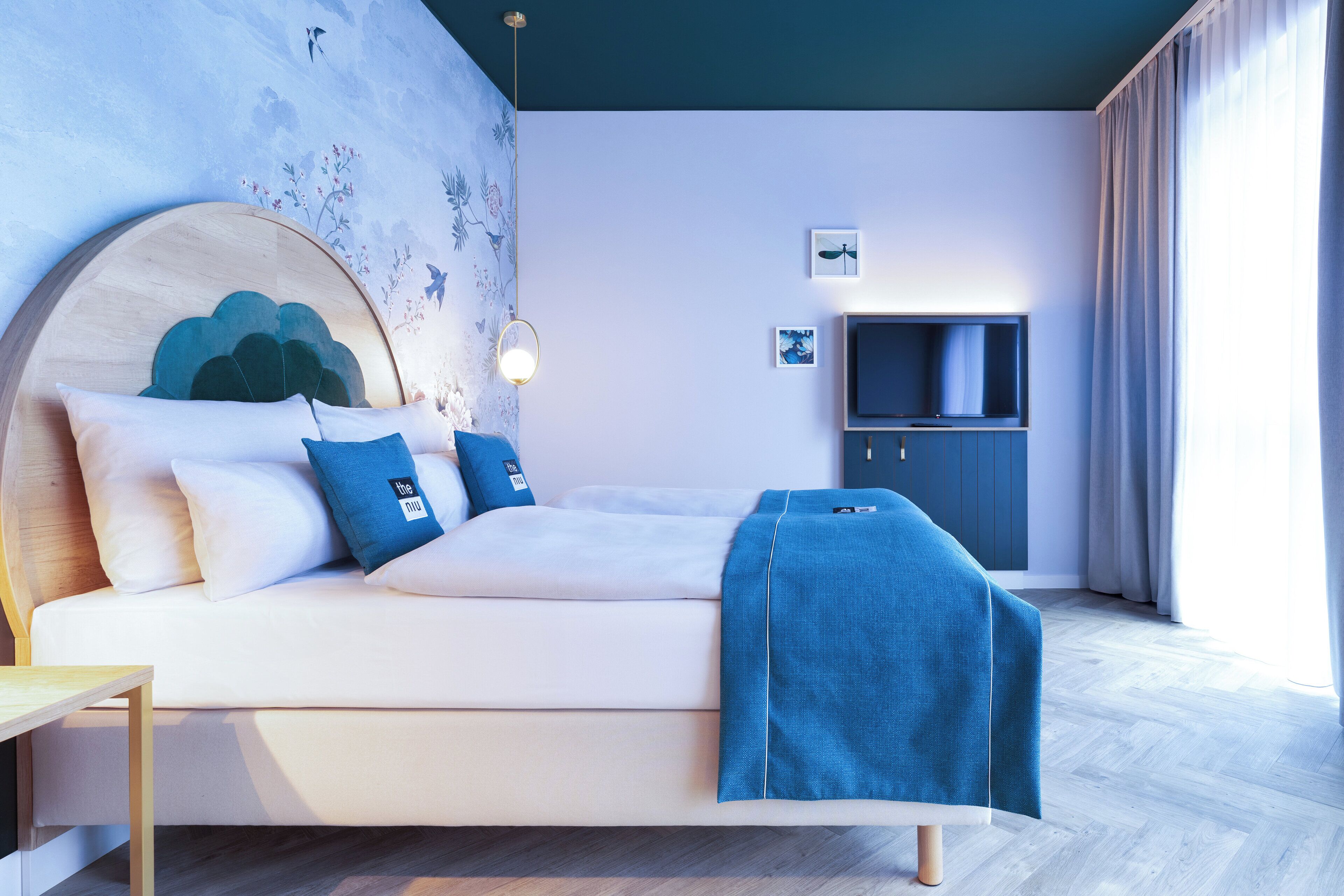 Une chambre moderne avec un lit, un téléviseur et un mur orné d’une fresque florale.