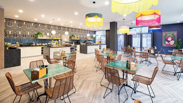 A modern restaurant with a central bar area, wicker chairs, and pendant lighting. - Holiday Inn - the niu, Flower Konstanz by IHG (Konstanz)