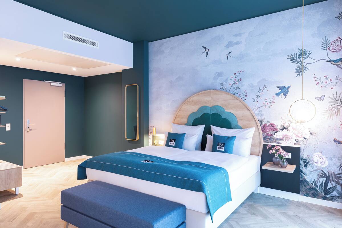 Un dormitorio moderno con una cama grande, cabecera de madera y un mural con pájaros y flores.