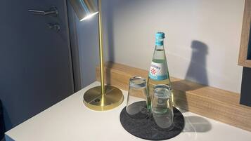 A modern bathroom with a white countertop, a bottle of Groseiner Medium, two clear glasses, and a gold-colored lamp.