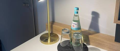 A modern bathroom with a white countertop, a bottle of Groseiner Medium, two clear glasses, and a gold-colored lamp.