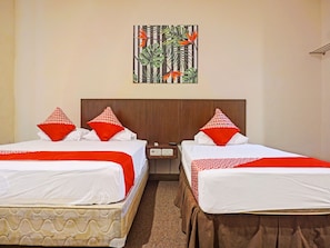 A hotel room with two beds, each with white bedding and red pillows, a wooden headboard, a nightstand with a phone and remote, and a painting of tropical foliage on the wall. - Collection O 91414 Hotel Marina Beach (Makassar)