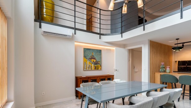 A modern dining area with a glass table and wicker chairs, a painting on the wall, and a kitchen in the background. - LF PARKING INCLUDED. Loft adjacent to Santa Cruz (Sevilla)