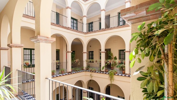 Un cortile a più livelli con archi e balconi, arricchito da piante in vaso e un pavimento piastrellato.