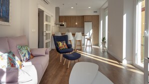 Una sala de estar moderna con sofá, sillas y un comedor, con una cocina al fondo.