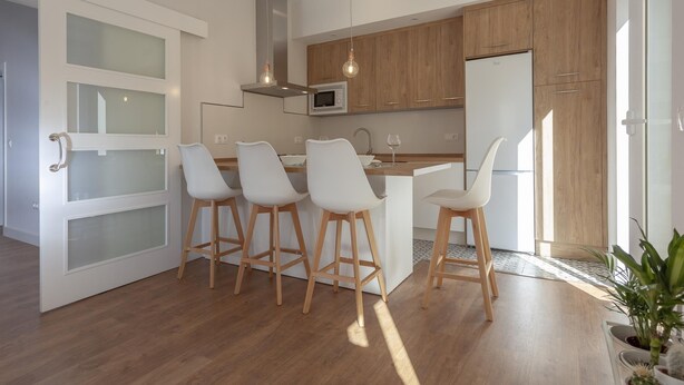 Una cocina moderna con armarios de madera, una isla central con taburetes altos y un microondas integrado.