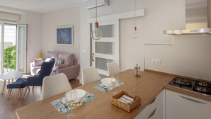 Una cocina moderna con encimera de madera, armarios blancos y una estufa a gas. Hay una zona de comedor con una mesa y sillas, y un sofá al fondo.