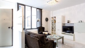 A modern living room with a sofa, coffee table, TV, bookshelf, and a large window. - LR2 PRIVATE TERRACE and parking included. Apartment in the Historic Center (Sevilla)
