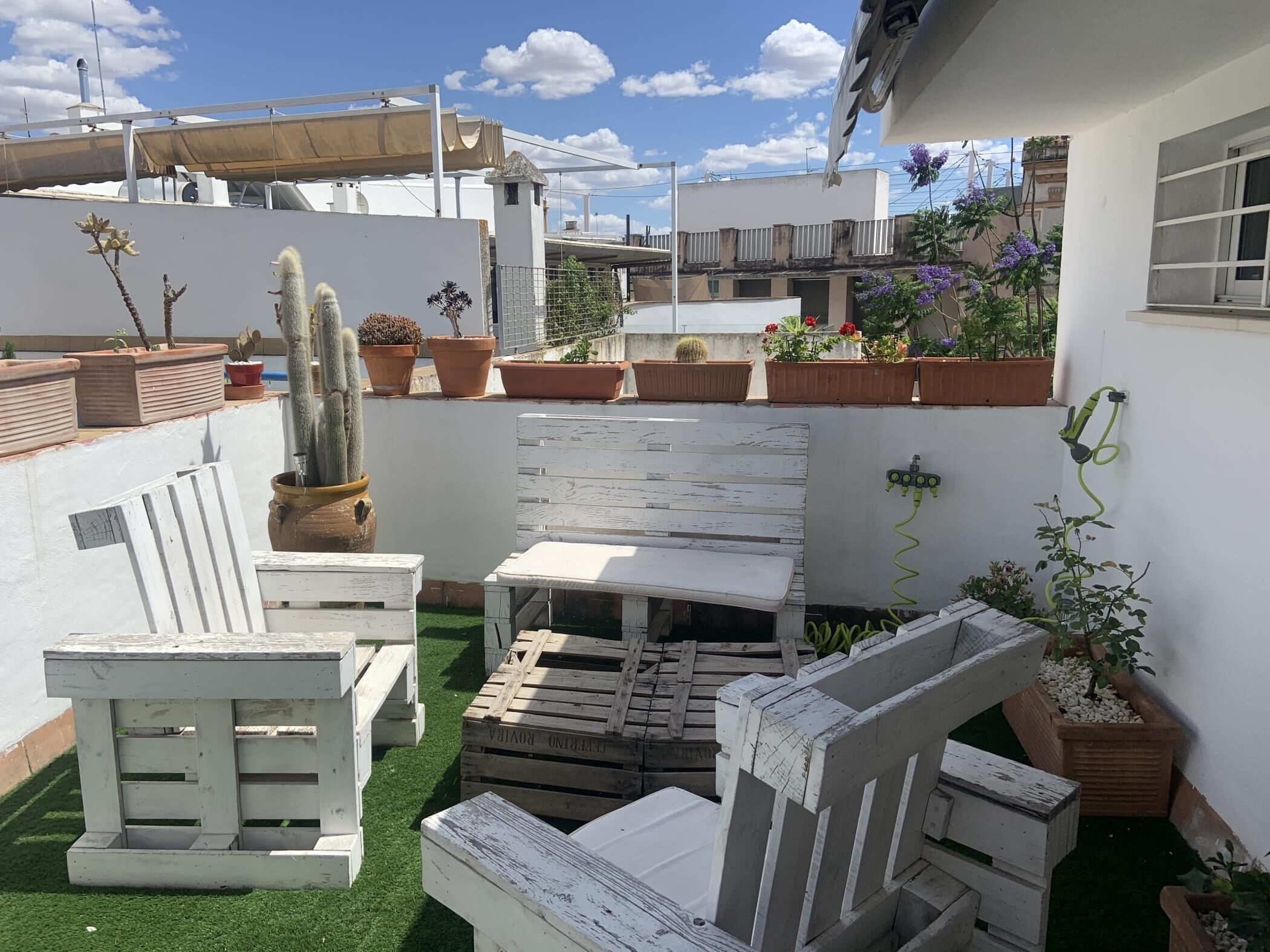 Een dakterras met potplanten, een houten bank en een witte tafel.