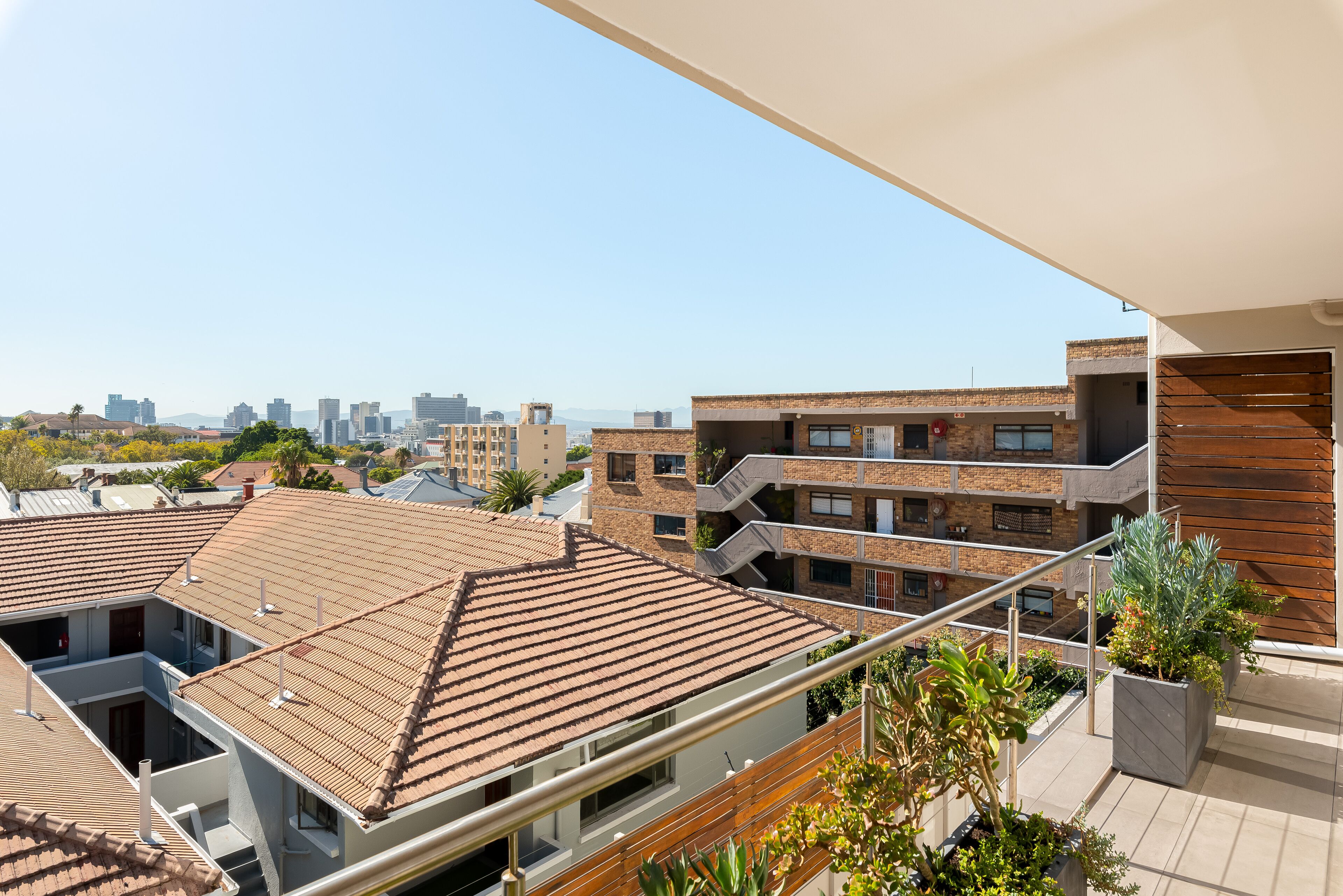 A residential building with a tiled roof, a balcony with potted plants, and a view of a city skyline.