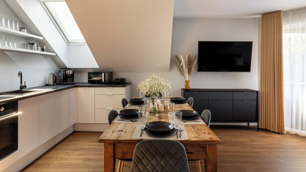 A modern kitchen with a dining area, a TV mounted on the wall, and a window with curtains. - Trevi Apartments Tychy (Tychy)
