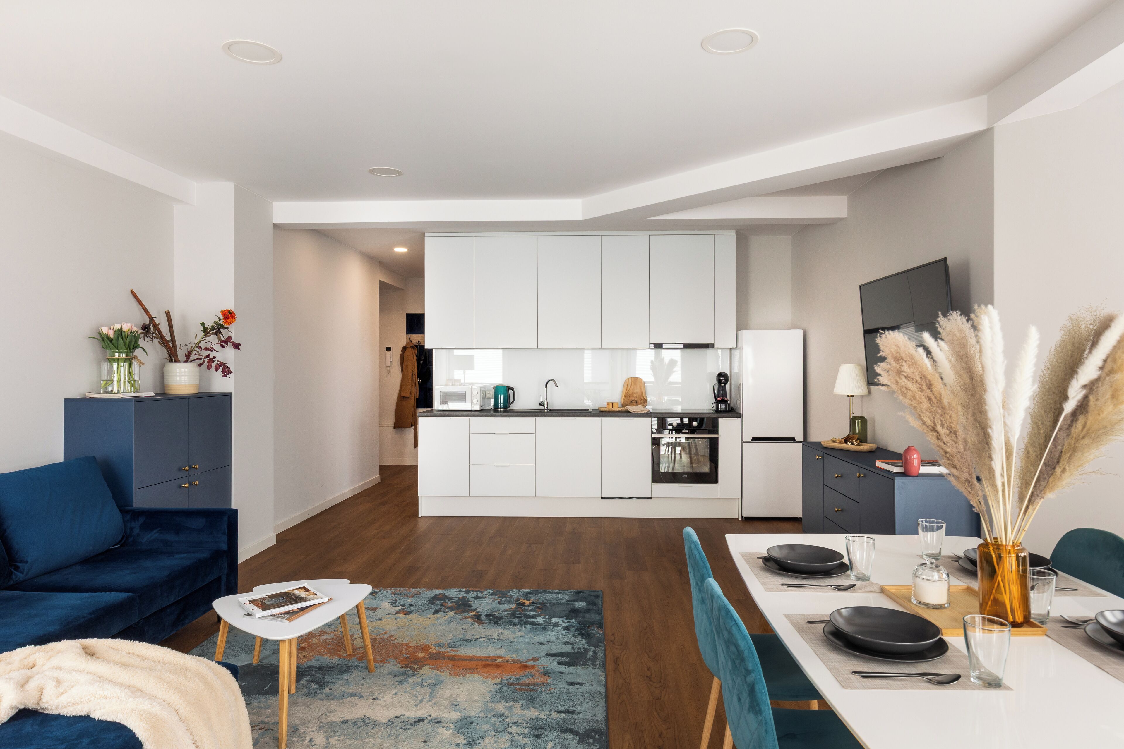Una sala de estar moderna con un sofá azul, una mesa de centro y un comedor con una mesa blanca para cuatro.