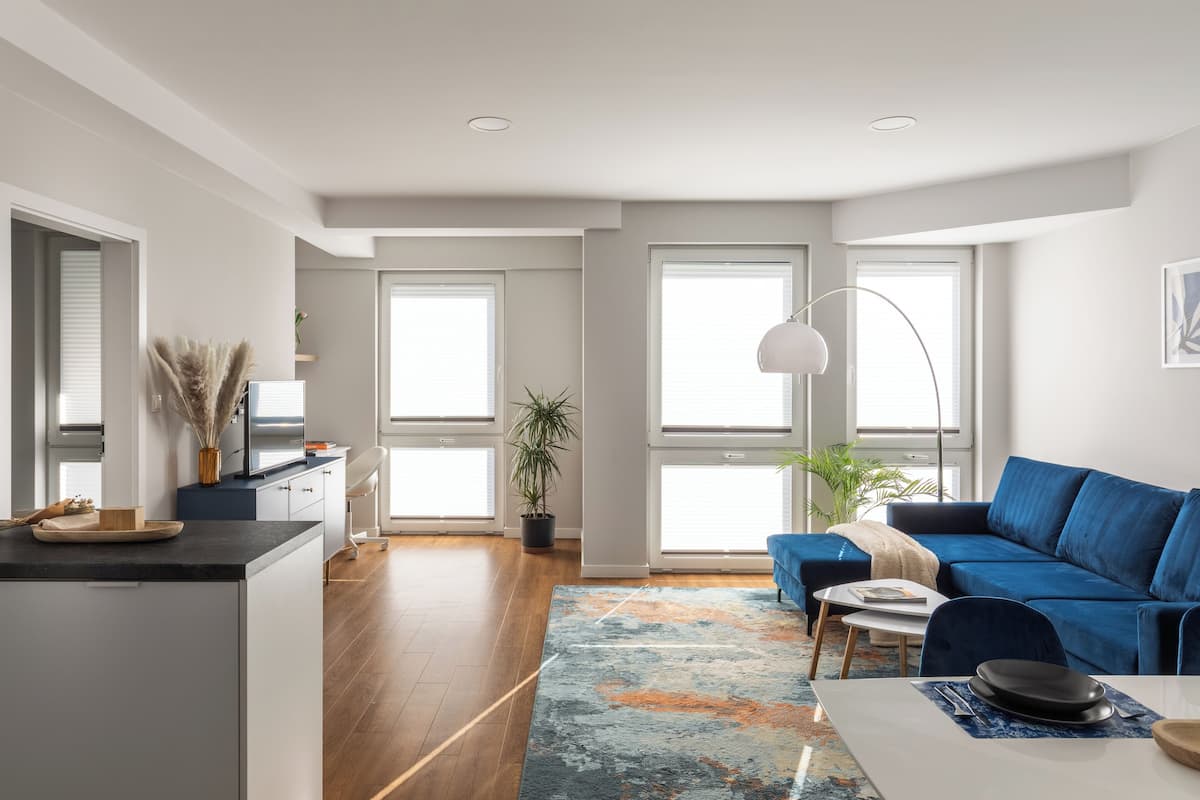 Una sala de estar moderna con un sofá azul, una mesa de centro y una alfombra. Hay una zona de cocina con una encimera y armarios.