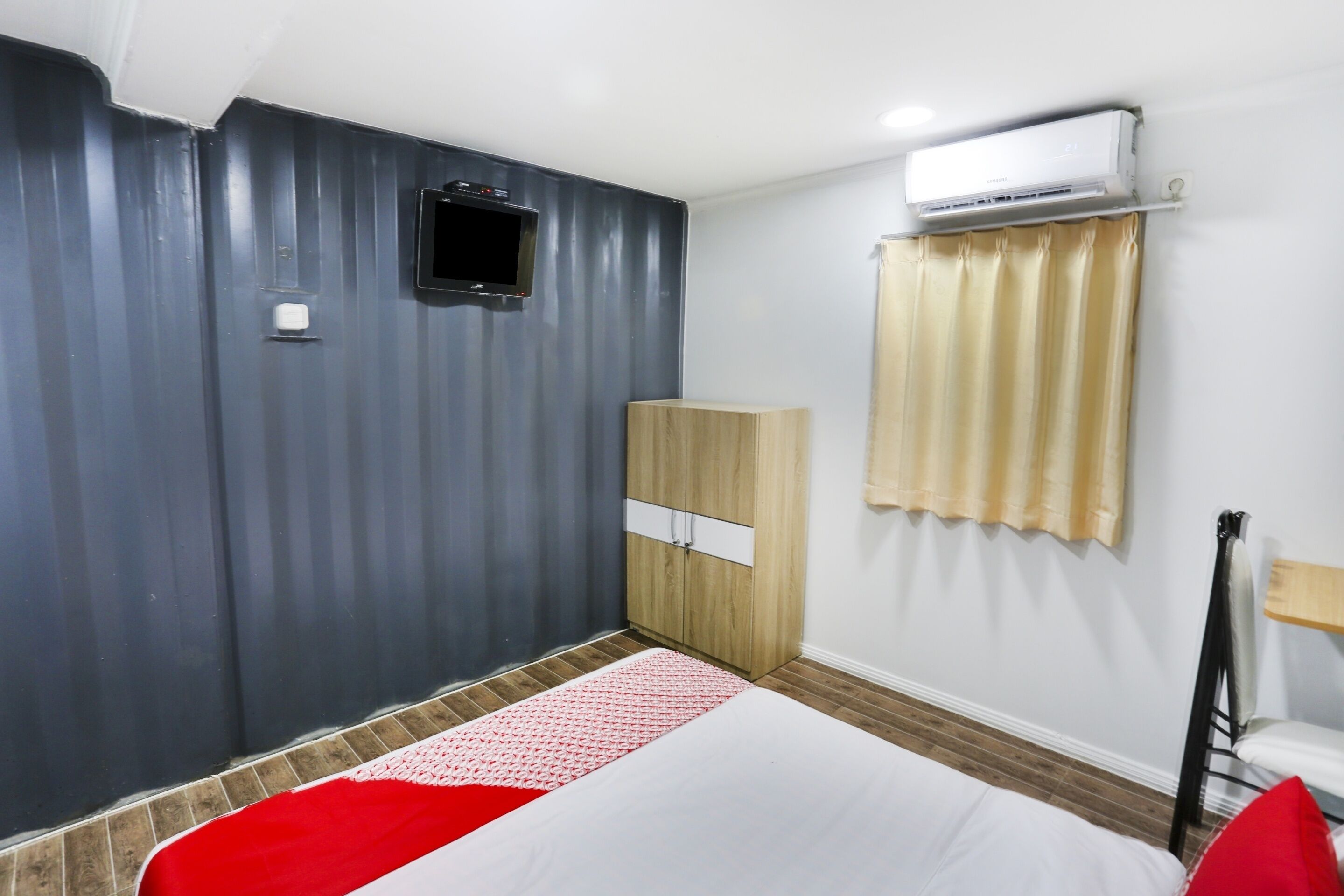 A hotel room with a bed, a wardrobe, a TV, and an air conditioning unit.