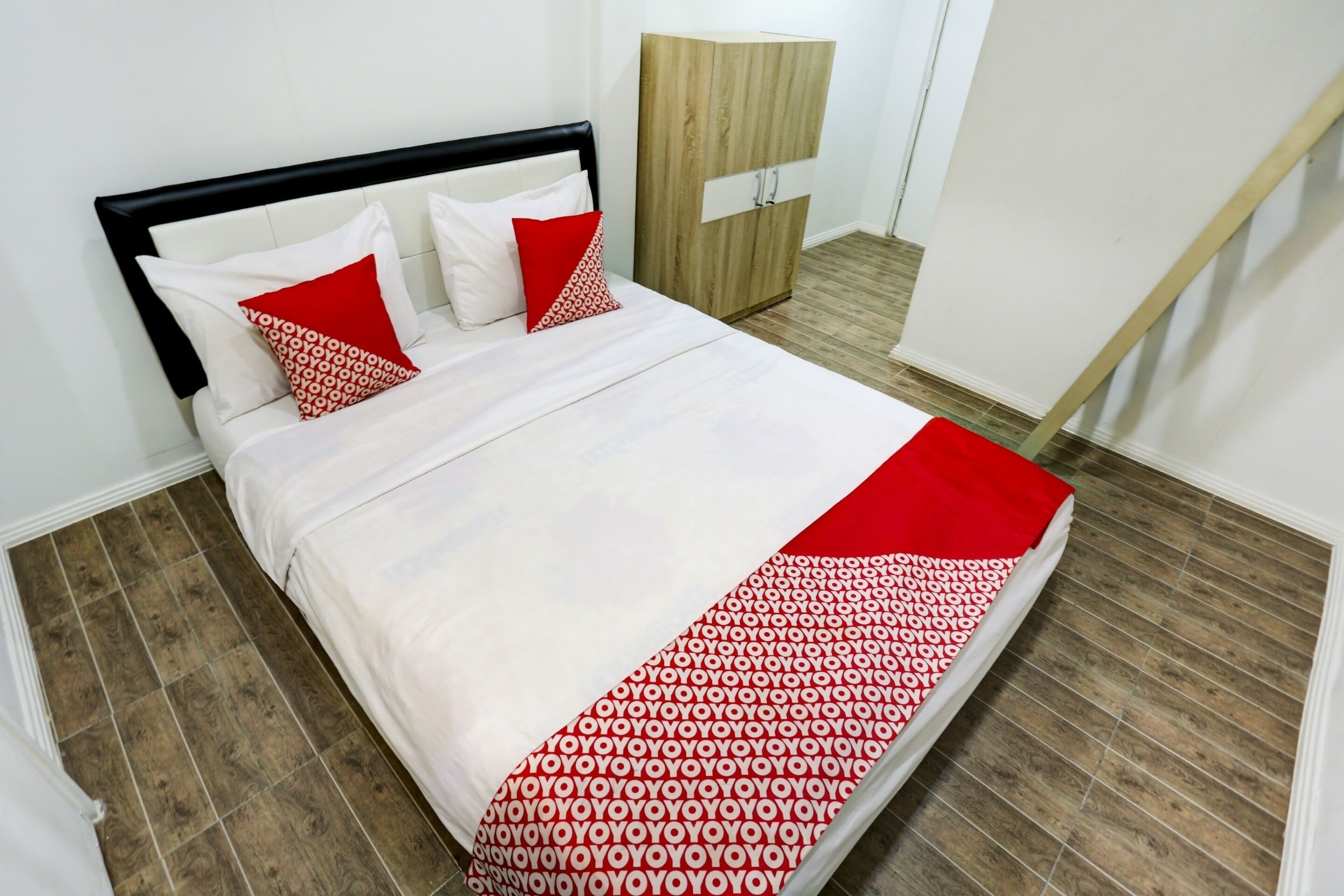 Una cama bien hecha con una colcha blanca y roja estampada, un cabecero negro y dos almohadas, una roja y otra blanca.