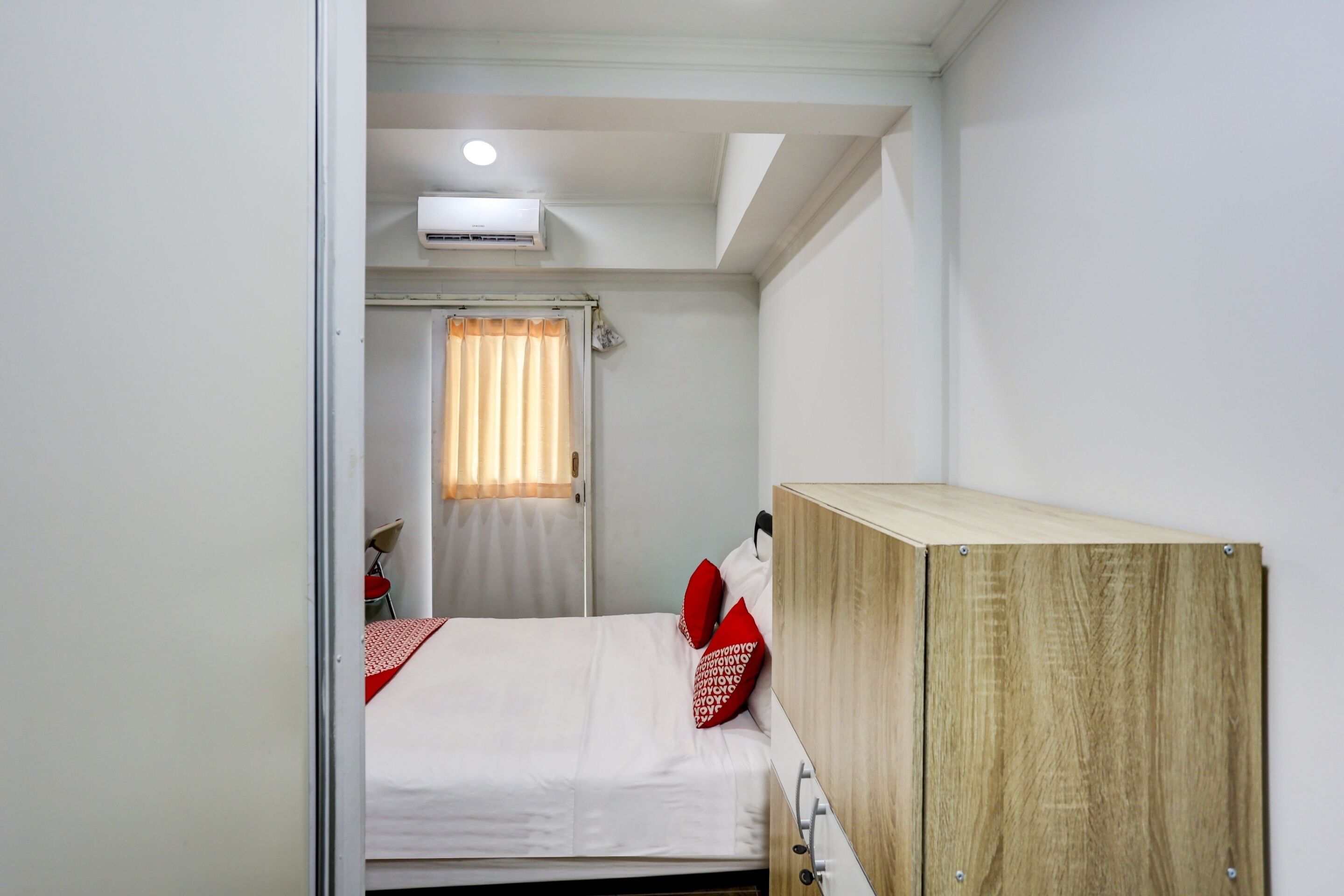 Une chambre à coucher avec un lit, une armoire en bois, un ventilateur de plafond et une fenêtre avec des rideaux.