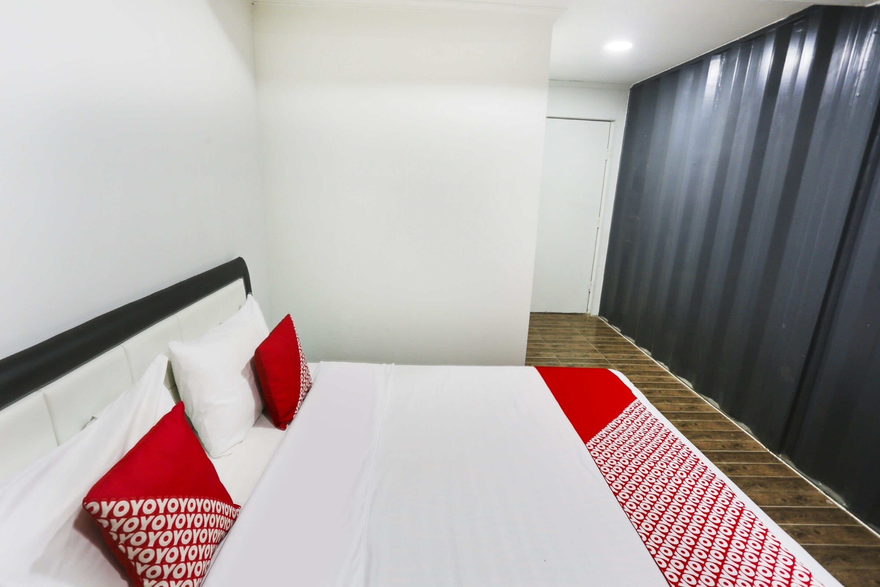 Habitación de hotel con cama, paredes blancas, cabecero negro y colcha con estampado rojo y blanco.