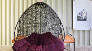 A hanging chair with a netted canopy and a cushioned seat, positioned in front of a wall with vertical panels and a framed picture. - Capital O 3300 Nadjara Residence Syariah (Pekanbaru)