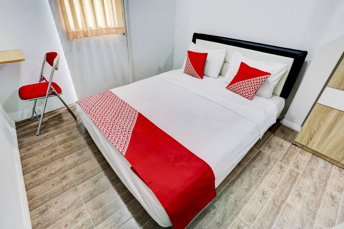 Un lit bien fait, avec une couvre-lit blanche et rouge, deux oreillers et un plaid rouge.