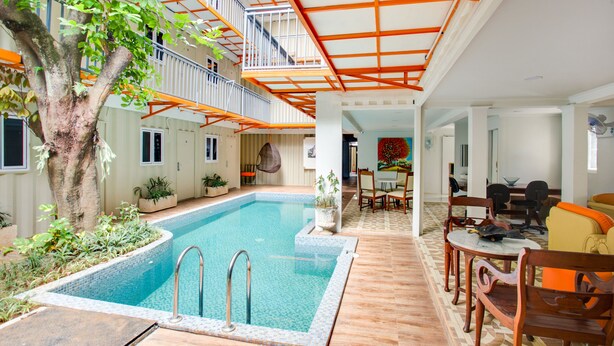 An indoor swimming pool with a tree, a dining area with chairs and a table, and a staircase with orange railings. - Capital O 3300 Nadjara Residence Syariah (Pekanbaru)