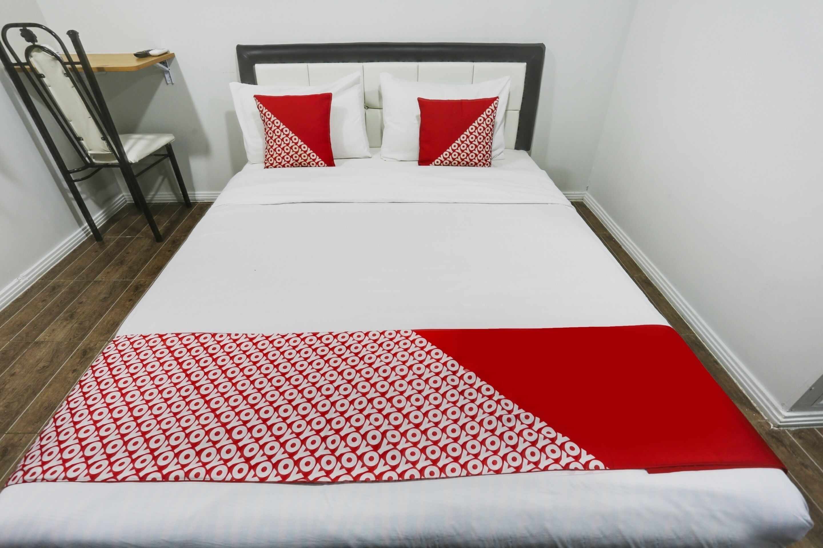 A neatly made bed with white and red bedding, a wooden nightstand, and a chair.