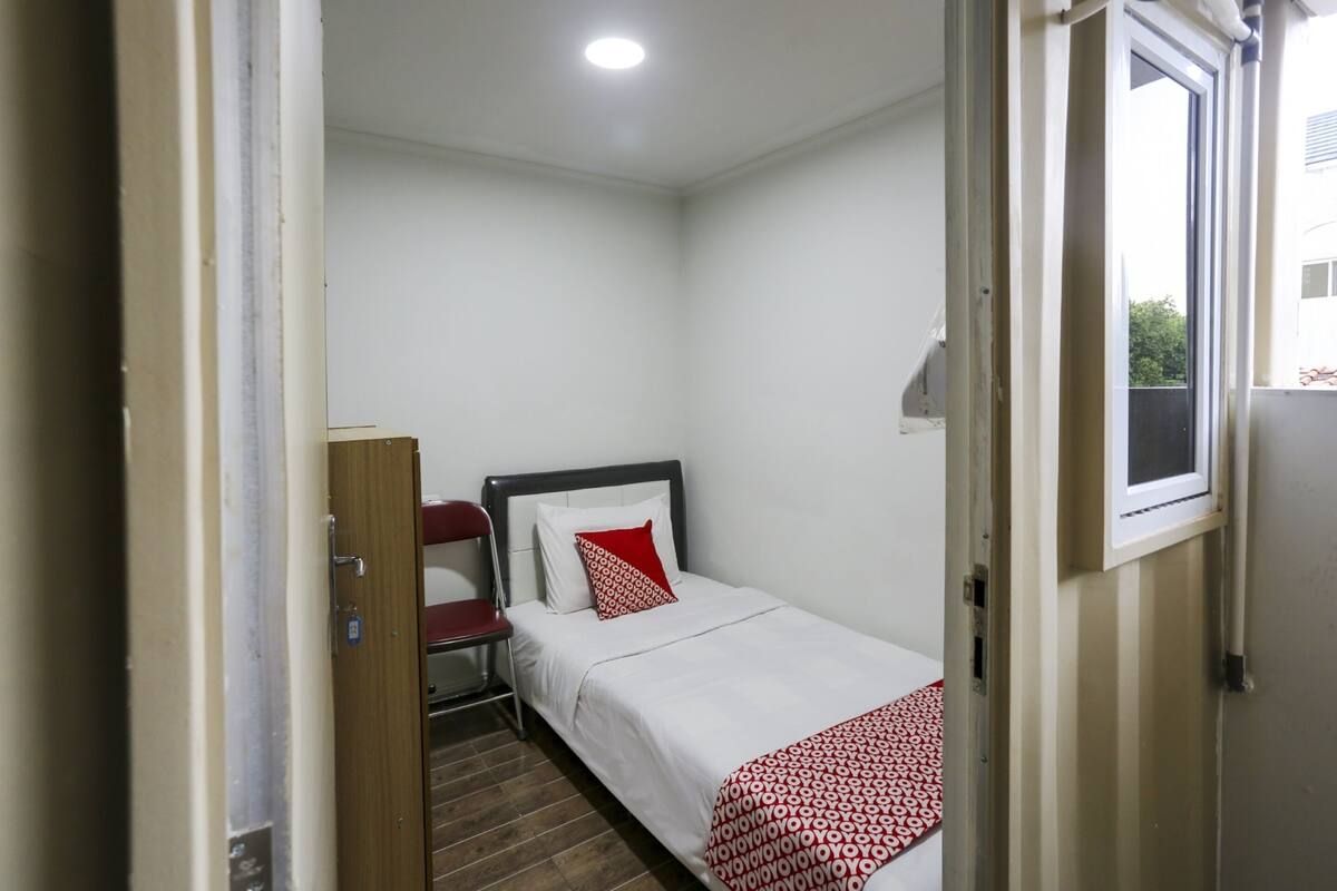 Une petite pièce propre, avec un lit, une chaise et une fenêtre.