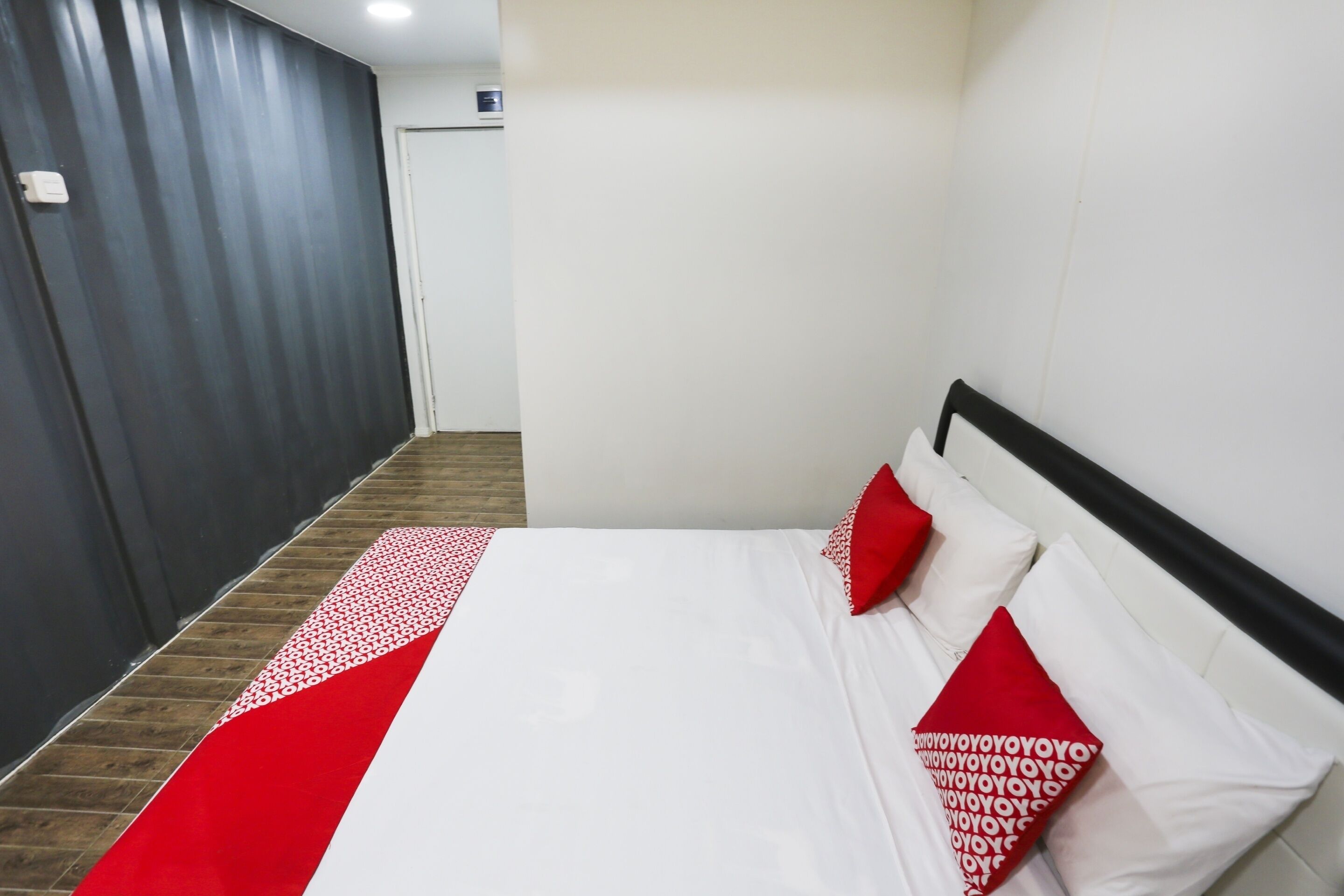 A hotel room with a bed, a red and white patterned bedspread, and red pillows.