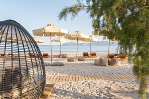 A beach with lounge chairs and umbrellas, a wooden deck, and a view of the sea and mountains. - Achilleas Beach Hotel Adults Only (Kos)